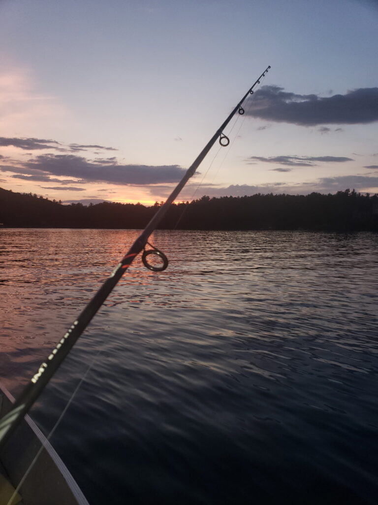 Fishing rod pointed across a lake at sunset before a night bass fishing trip.