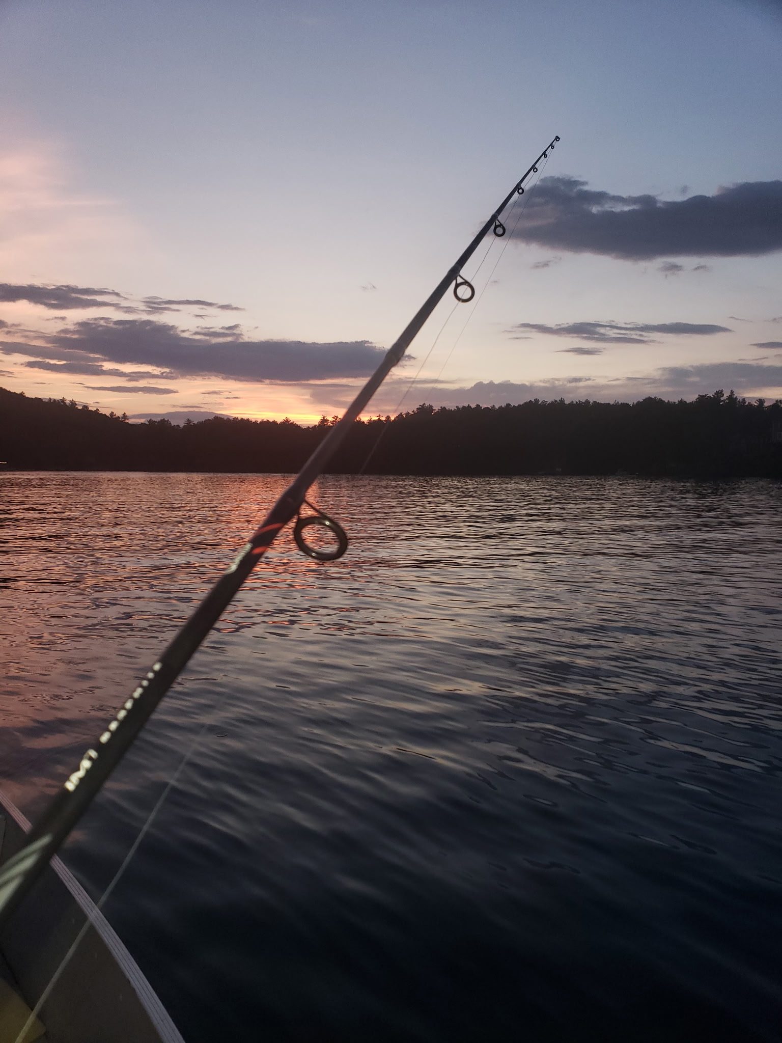 Fishing rod pointed across a lake at sunset before a night bass fishing trip.