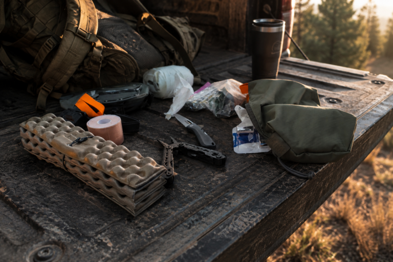 Underrated outdoor gear essentials on a truck tailgate including a multi-tool, organization bags, tape, and everyday hunting gear